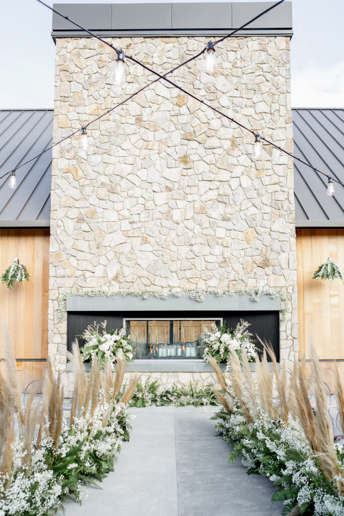 Estate Yountville wedding ceremony aisle with floral-lined walkway and stone fireplace backdrop in Napa Valley.
