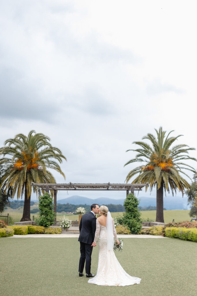 Bride and groom portrait at Carneros Resort and Spa standing beneath the ceremony arbor with palm trees and sweeping Napa Valley views