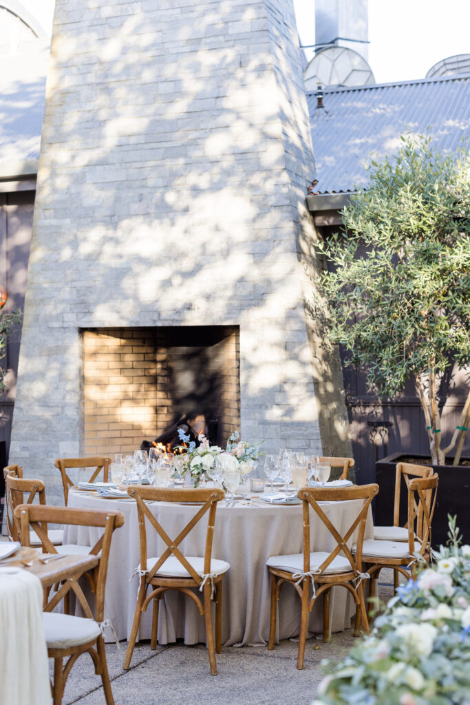Intimate wedding reception seating near the stone fireplace at Carneros Resort and Spa with round tables, wooden chairs, and romantic Napa Valley garden ambiance