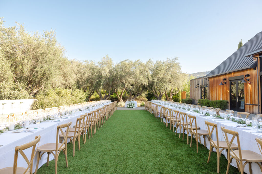 Outdoor wedding reception at Estate Yountville with long farm tables set beneath olive trees, photographed by a Napa Valley wedding photographer.