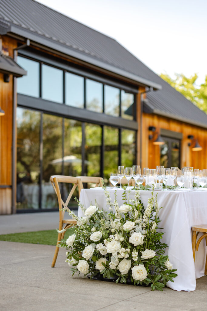 White floral arrangement with roses and greenery beside a reception table at Estate Yountville wedding in Napa Valley.