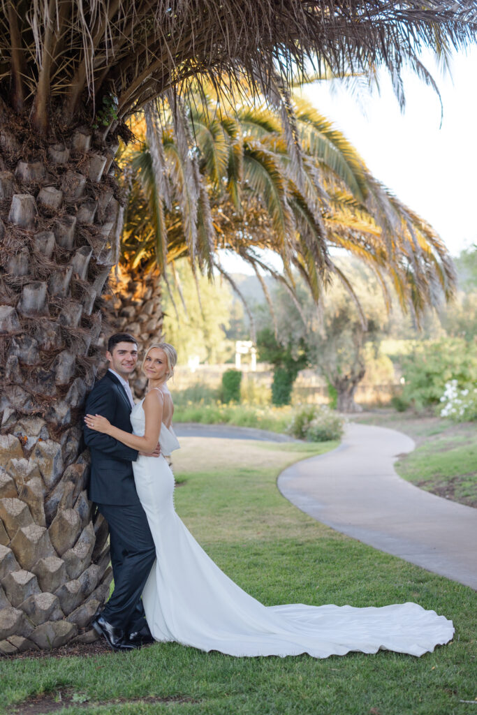 Bride and groom embracing beneath a palm tree at Estate Yountville in Napa Valley, captured by a wedding photographer familiar with the venue.