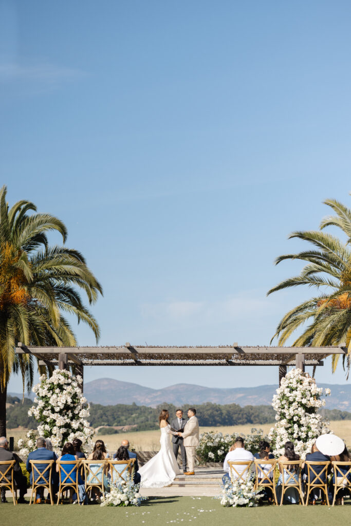 Outdoor wedding ceremony at Carneros Resort and Spa featuring a couple at the altar under the arbor with guests seated and Napa Valley hills in the background