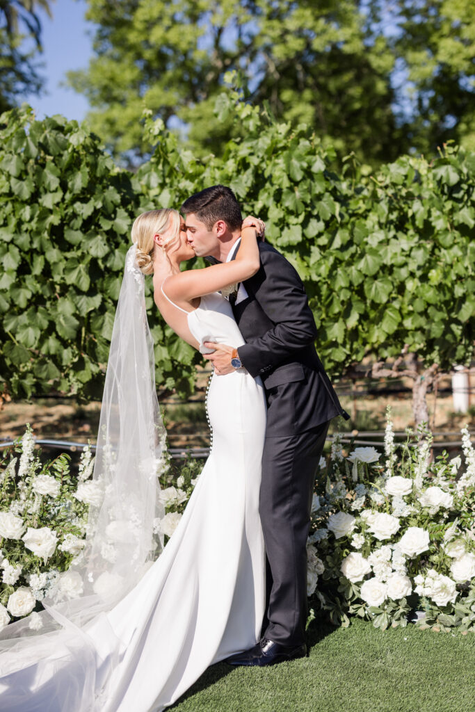 Bride and groom sharing a kiss among the vineyards at Estate Yountville during a sunlit Napa Valley wedding, photographed by an Estate Yountville wedding photographer.
