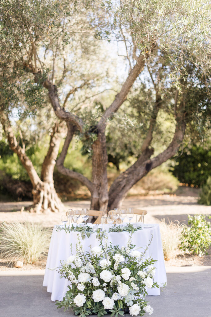 Sweetheart table styled with white florals and greenery beneath olive trees at Estate Yountville wedding in Napa Valley