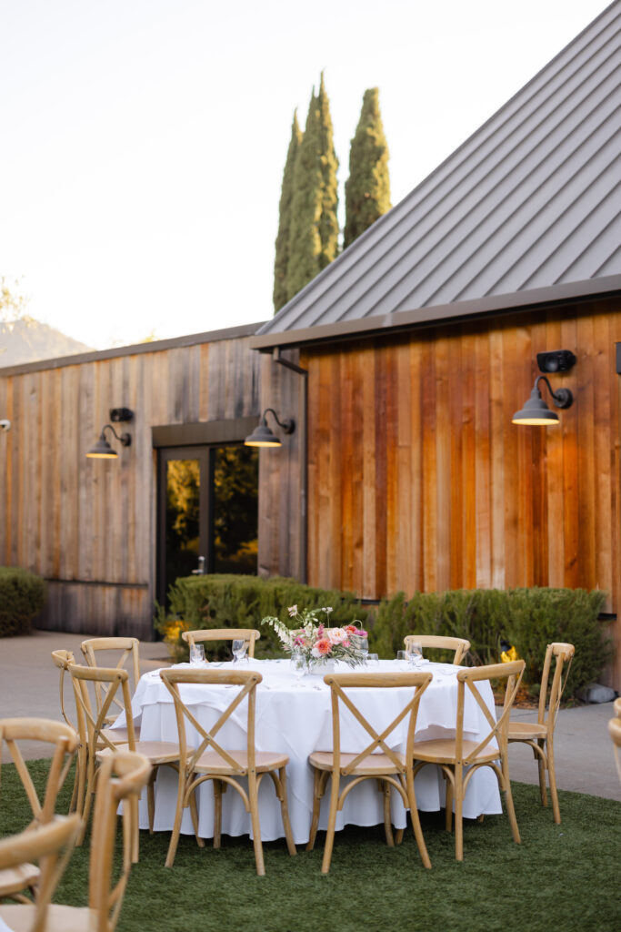 Outdoor wedding reception table set with white linens and wooden chairs beside the Estate Yountville event space.