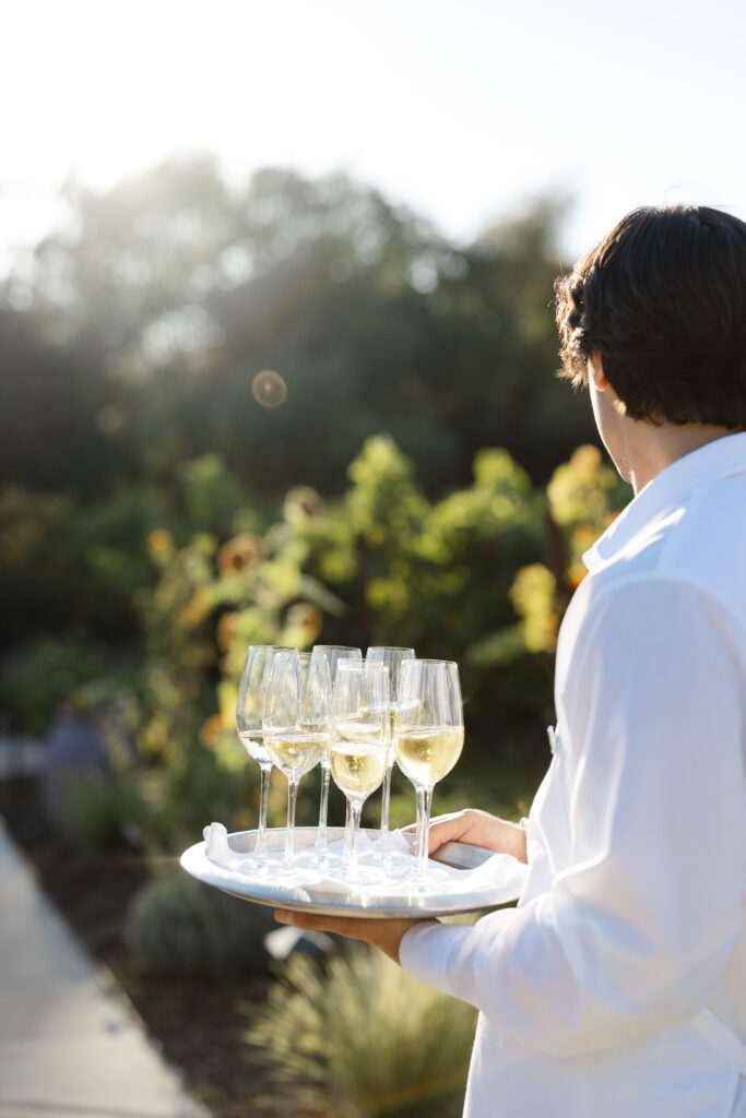 Server holding a tray of champagne glasses during golden hour at an Estate Yountville wedding reception in Napa Valley.