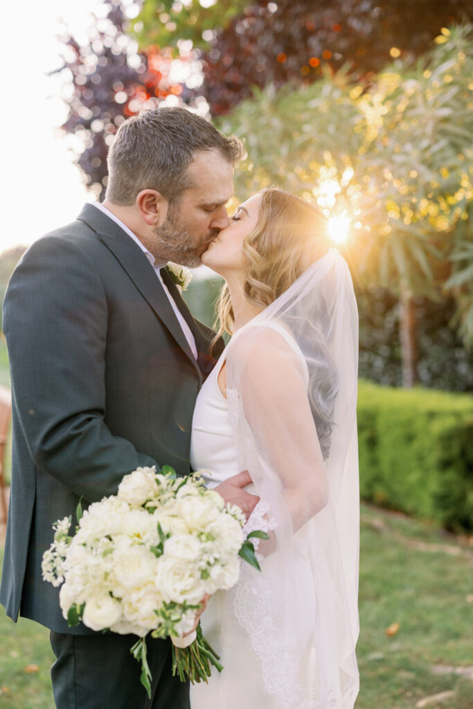 Bride and groom sharing a sunset kiss at Carneros Resort and Spa in Napa Valley, wedding bouquet in soft golden light