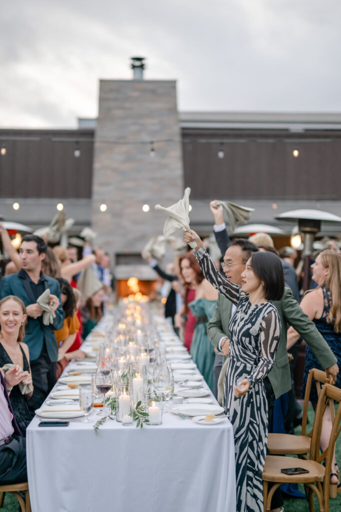 Guests waving napkins during a lively wedding reception at Carneros Resort and Spa with long tables, candlelight, and wine country ambiance in Napa Valley