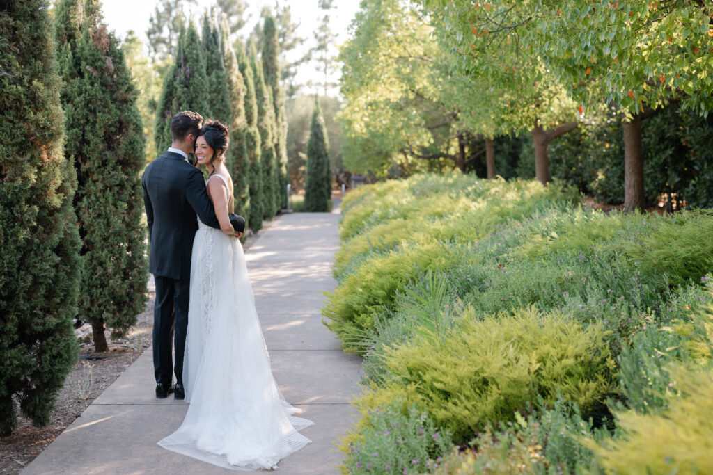 Newlyweds standing together on a garden walkway at Carneros Resort and Spa, surrounded by lush greenery in Napa Valley Wine Country.