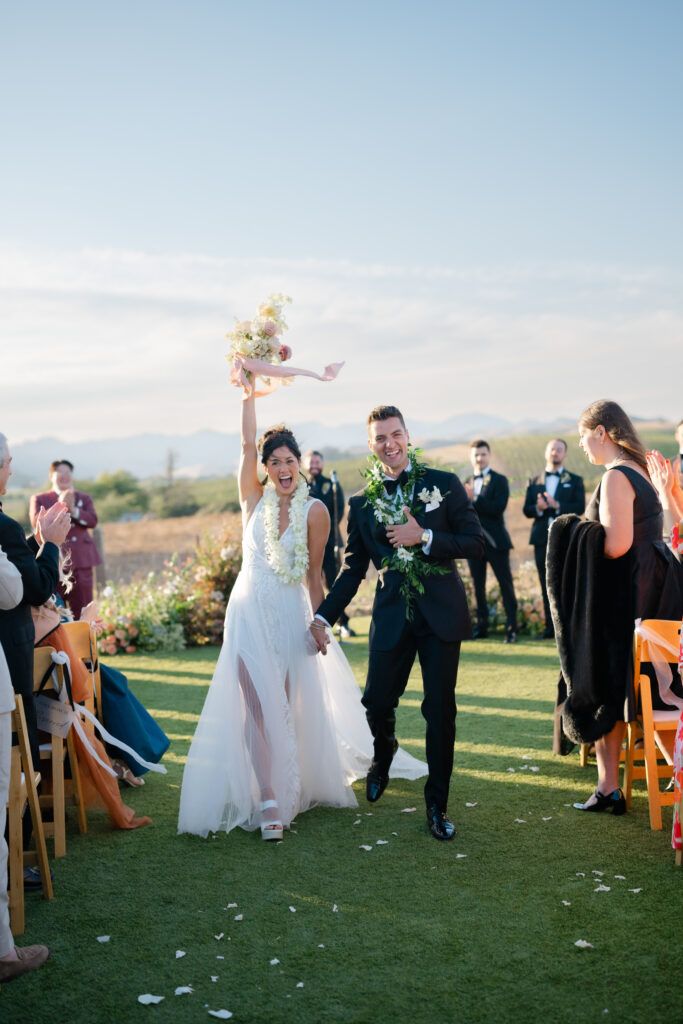 Newlyweds celebrating as they walk back down the aisle after their ceremony at the Hilltop Lawn at Carneros Resort and Spa in Napa Valley Wine Country.