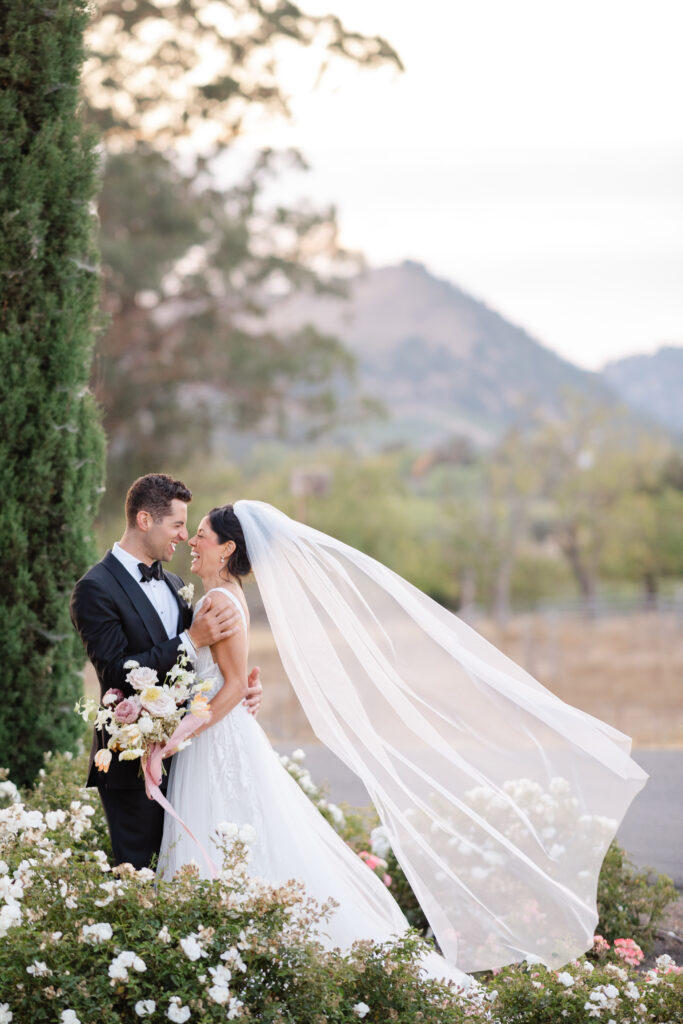 Bride and groom laughing together as the bride’s veil flows in the wind during golden hour portraits at Carneros Resort and Spa in Napa Valley