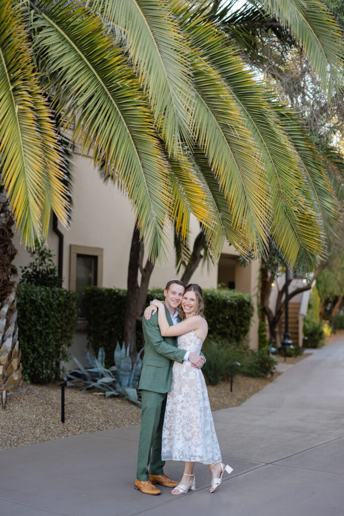 Bride and groom embracing beneath palm trees at Estate Yountville, surrounded by Mediterranean landscaping and soft afternoon light.