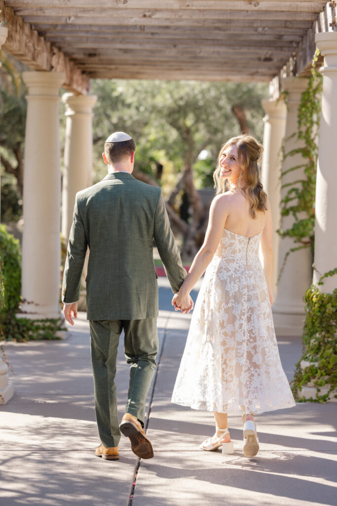 Bride and groom walking hand in hand through a vine-covered pergola at Estate Yountville, captured in warm natural light.