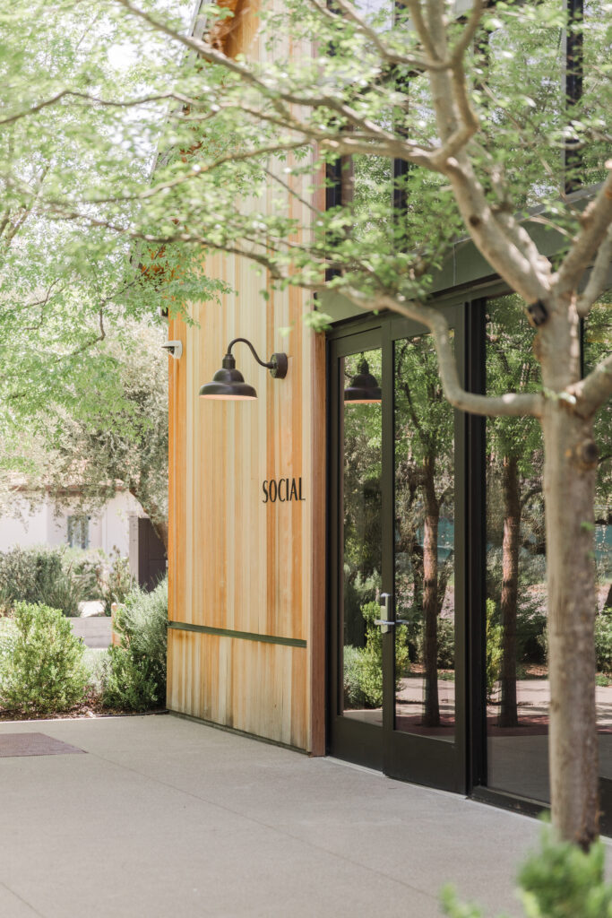 Entrance to The Social at Estate Yountville with glass doors, wood exterior, and surrounding greenery
