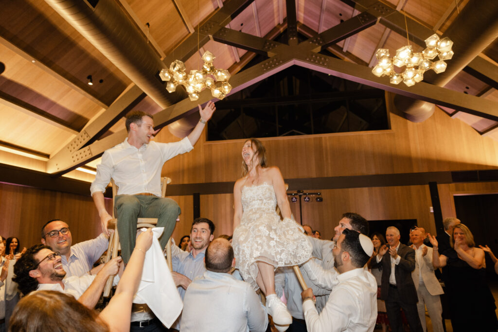Bride and groom lifted in chairs during a lively hora dance inside The Social at Estate Yountville wedding reception