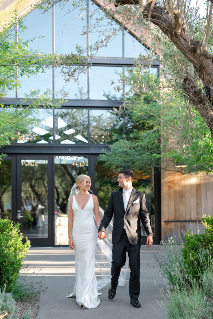 Bride and groom walking outside The Social at Estate Yountville surrounded by greenery and glass architecture