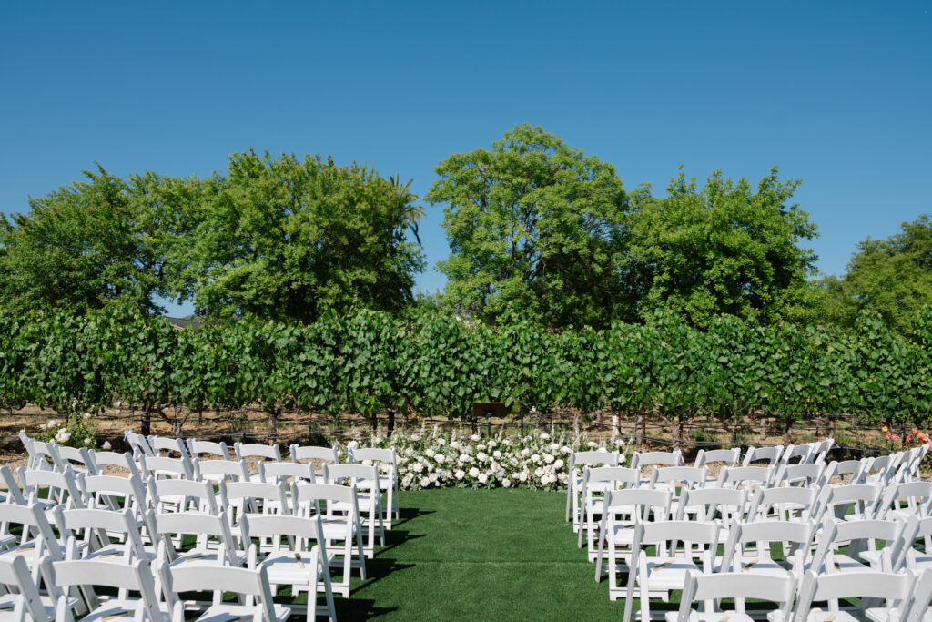 Outdoor wedding ceremony set in the vineyard at Estate Yountville, with rows of white chairs and lush Napa Valley vines