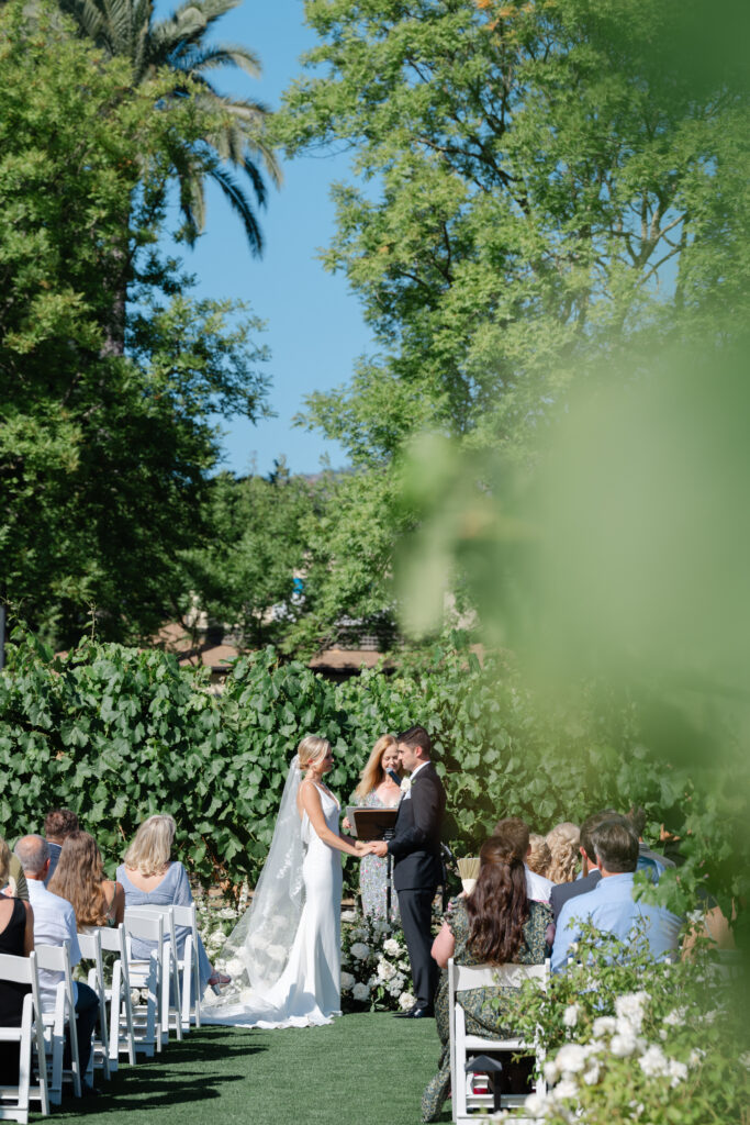Outdoor vineyard wedding ceremony at Estate Yountville, with the couple exchanging vows surrounded by Napa Valley greenery
