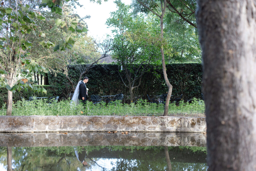 A bride and groom walk together beside a reflecting pond surrounded by mature trees during their Napa Valley wedding, photographed by Napa wedding photographer Suzanne Karp
