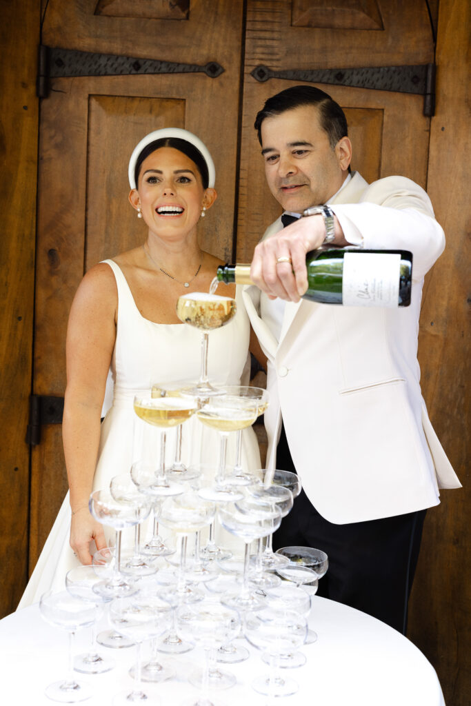 A bride and groom laugh together while pouring champagne into a coupe tower during their Napa Valley wedding reception, photographed by Napa wedding photographer Suzanne Karp
