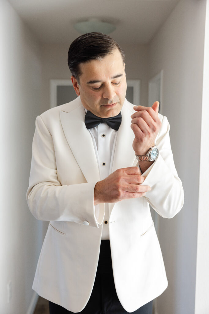  A groom in a white tuxedo jacket fastens his cufflinks while getting ready for his Napa Valley wedding, photographed by Suzanne Karp Photography
