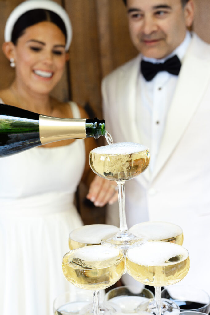  Champagne is poured into a coupe tower as a bride and groom celebrate their Napa Valley wedding reception, photographed by Napa wedding photographer Suzanne Karp