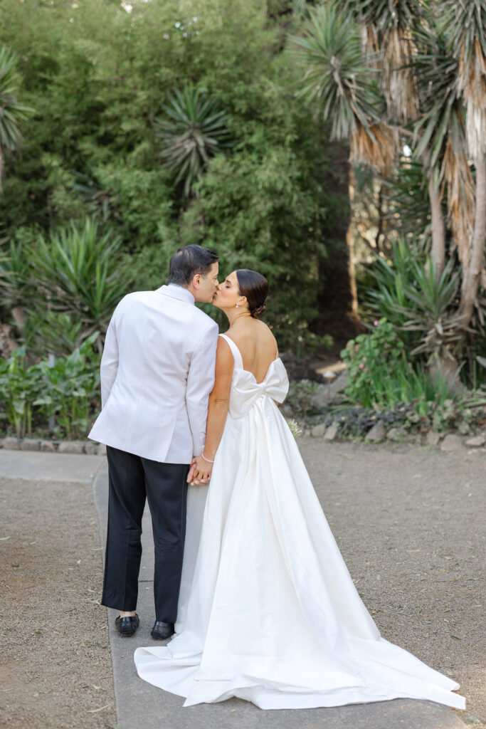A bride and groom share a kiss during their Napa Valley wedding portraits, the bride wearing a gown with a dramatic bow back, photographed by Napa wedding photographer Suzanne Karp