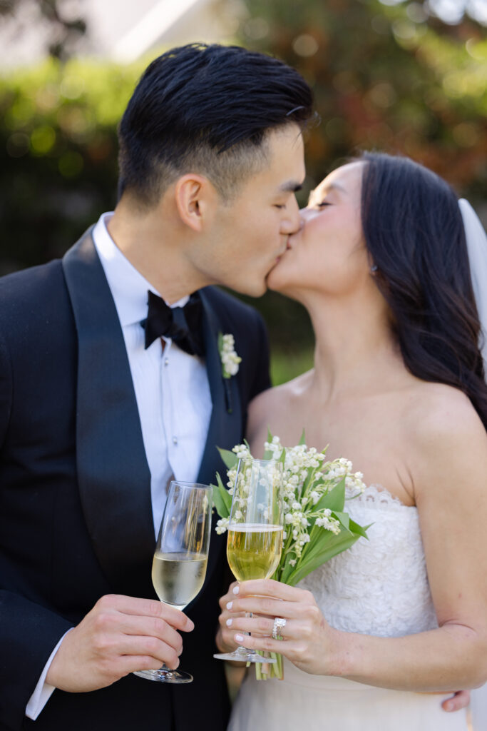 A bride and groom share a close up kiss during cocktail hour at their Napa Valley wedding, the bride holding her bouquet and a glass of champagne, photographed by Suzanne Karp Photography
