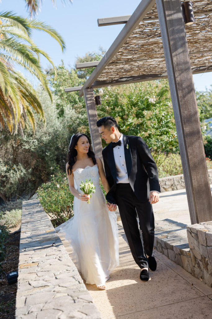 A bride and groom walk hand in hand beneath the iconic pergola at Carneros Resort and Spa during their Napa Valley wedding portraits, photographed by Napa wedding photographer Suzanne Karp
