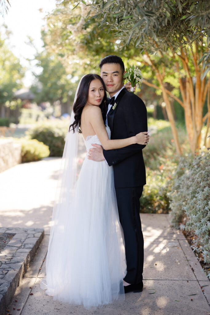 A bride and groom embrace among the lush gardens at Carneros Resort and Spa during their Napa Valley wedding portraits, photographed by Suzanne Karp Photography