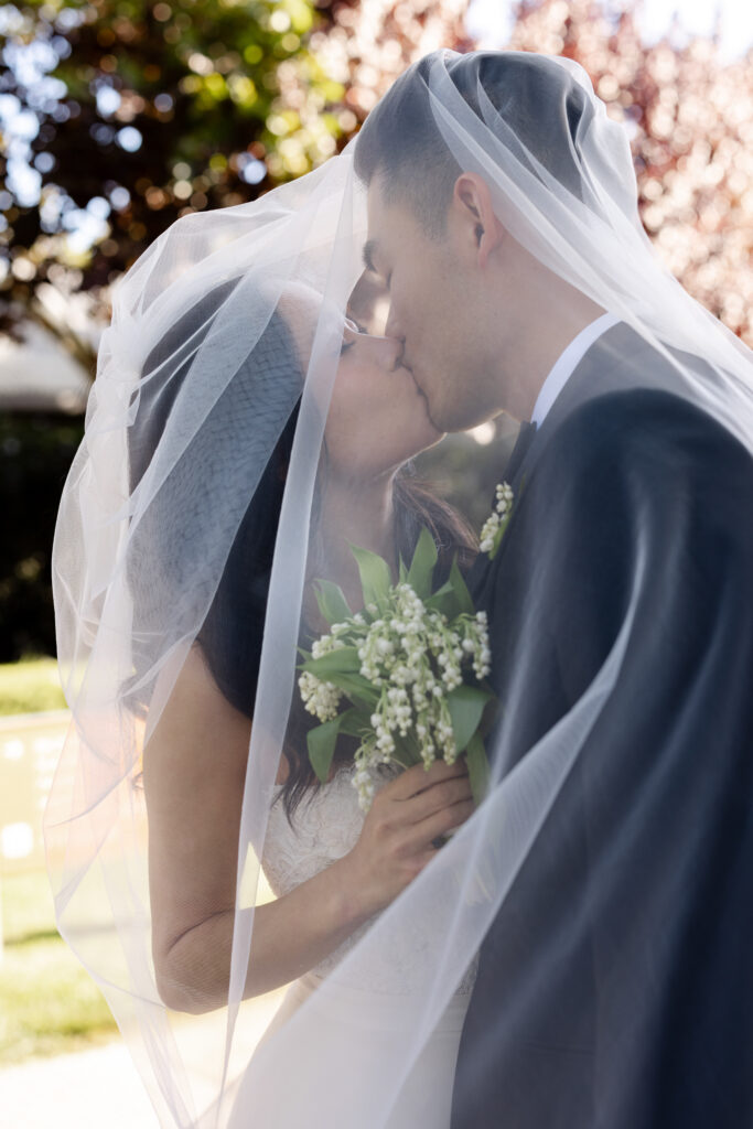 A bride and groom share a romantic kiss wrapped together beneath her flowing veil during their Napa Valley wedding portraits, photographed by Napa wedding photographer Suzanne Karp