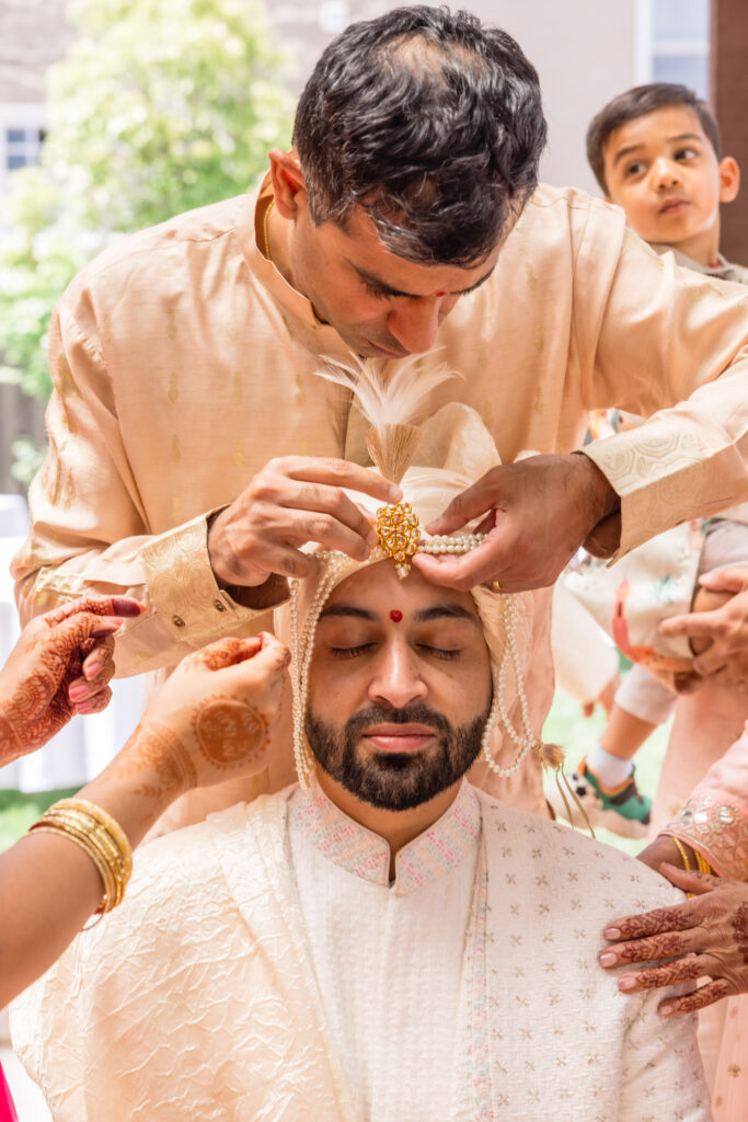 Family members place a pearl and gold sehra on the groom's head during his Hindu wedding ceremony at a private Napa Valley estate, photographed by Napa Valley wedding photographer Suzanne Karp