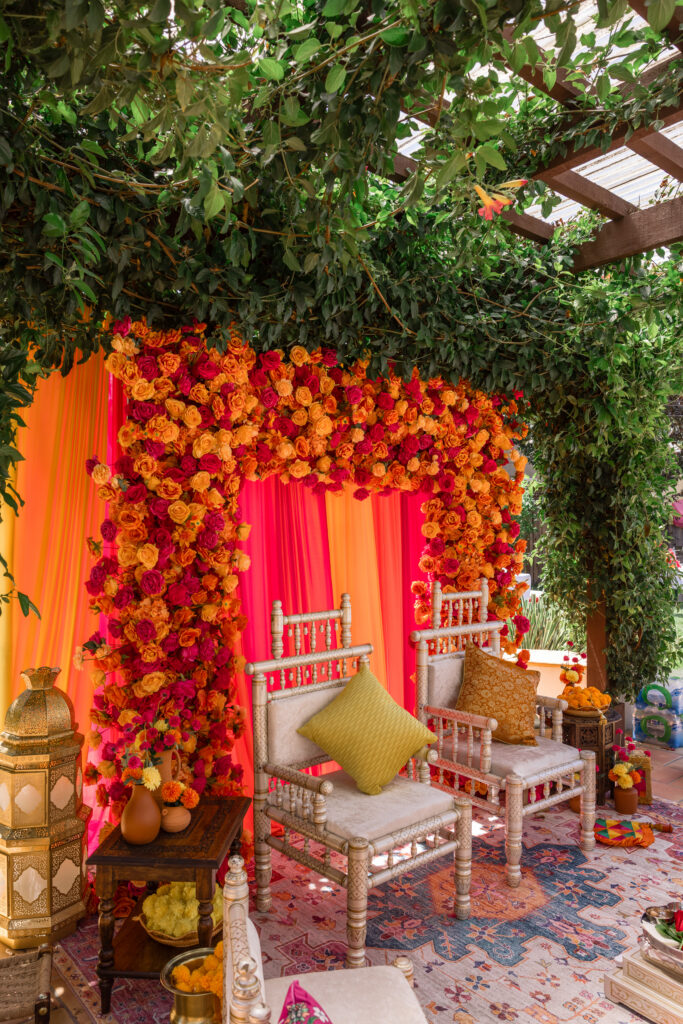 A vibrant Hindu wedding mandap dressed in orange and fuchsia roses with silk flame-toned draping and gilded ceremonial chairs at a private estate, photographed by Napa Valley wedding photographer Suzanne Karp