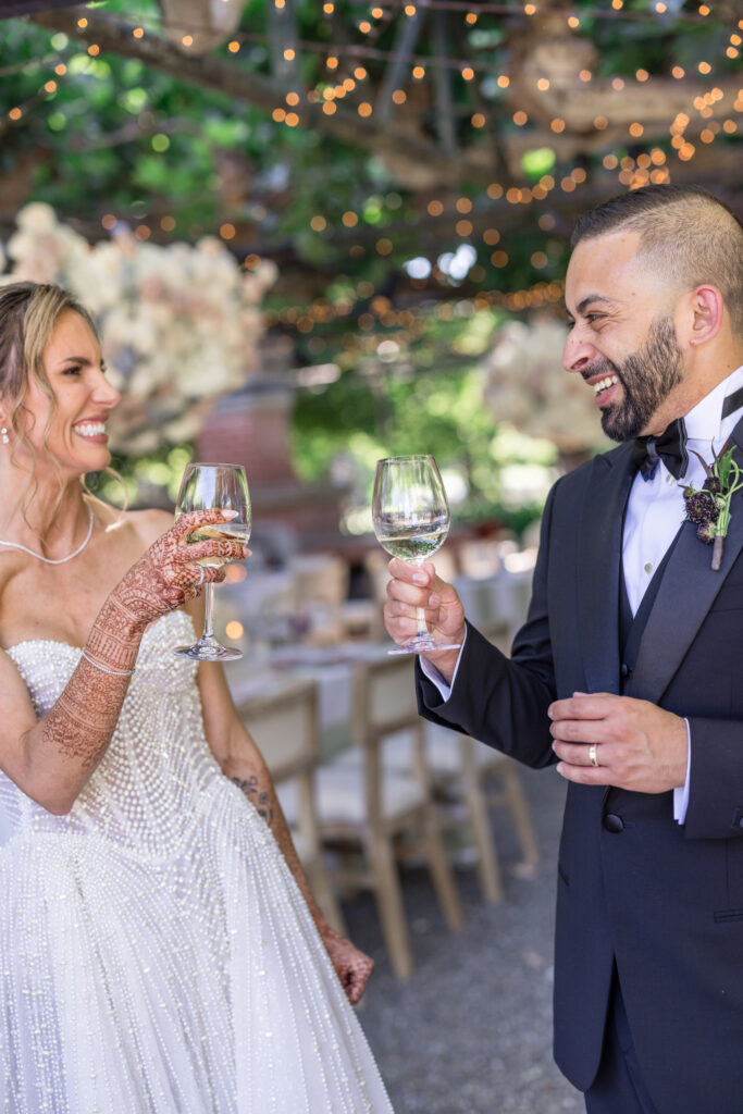 A bride and groom share a champagne toast beneath the fig tree trellis at Beaulieu Gardens in Rutherford during their Napa Valley wedding reception, photographed by Suzanne Karp Photography