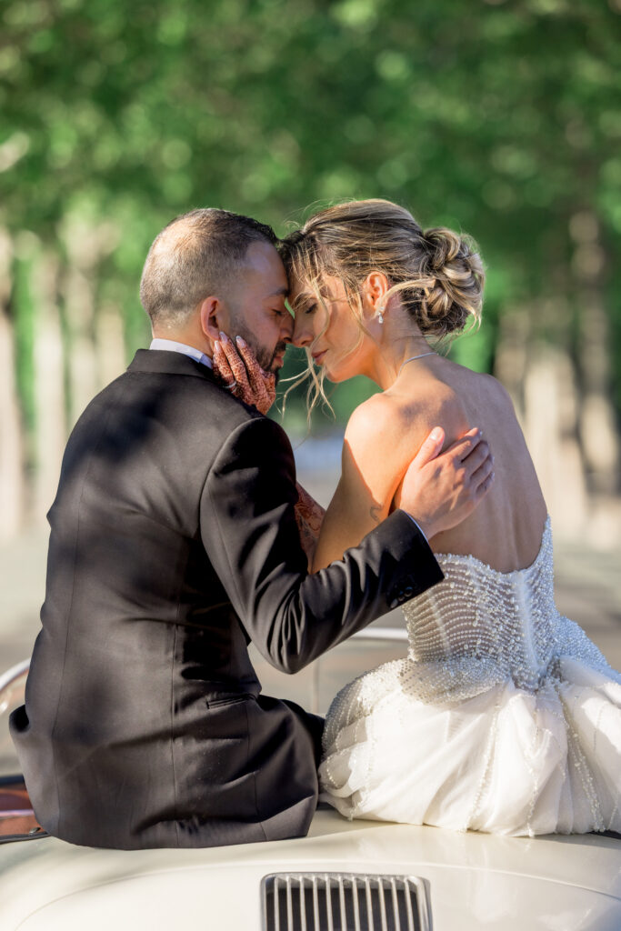 A bride and groom share a kiss while seated in a vintage white Porsche convertible surrounded by vineyard trees during their Napa Valley wedding, photographed by Suzanne Karp Photography