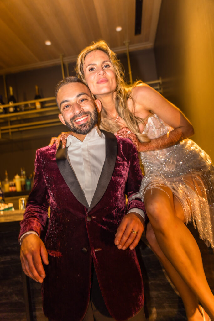 A bride in a beaded fringe reception dress and groom in a burgundy velvet blazer laugh together at the after party during their multi-day Napa Valley wedding celebration at Estate Yountville, photographed by Napa Valley wedding photographer Suzanne Karp