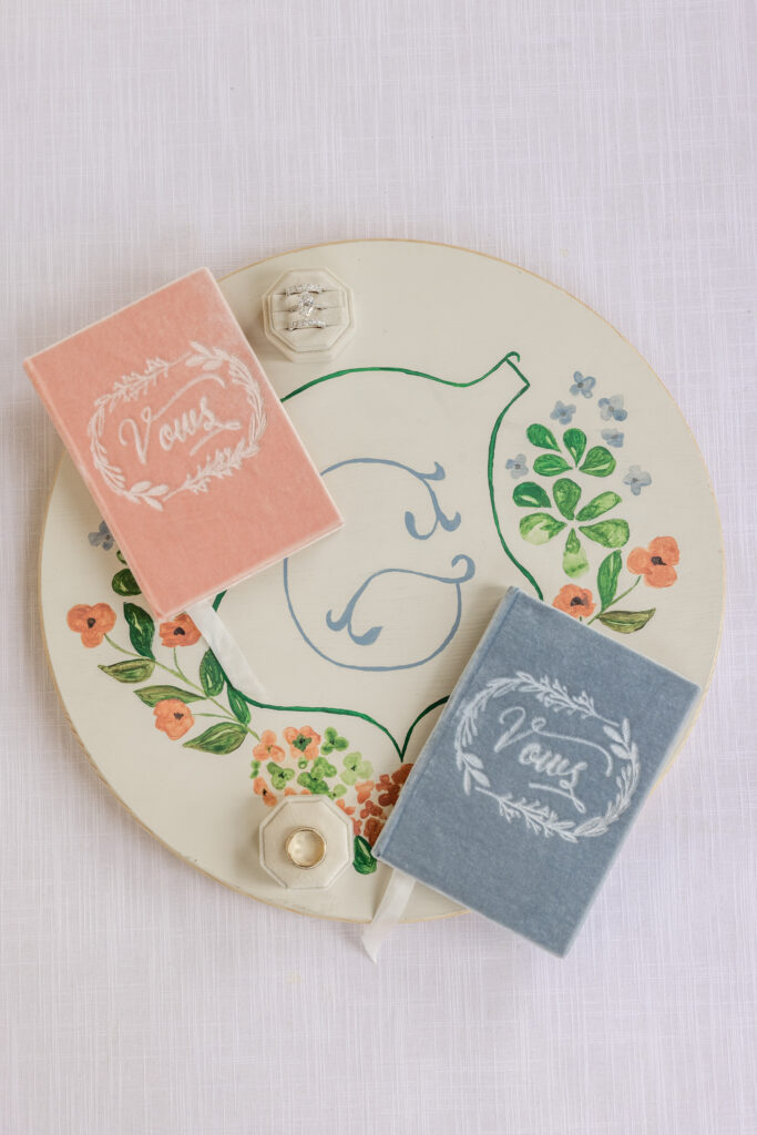 A close up detail of hand lettered vow books and a gold ring resting on a painted ceramic plate during wedding day preparations for a Napa Valley wedding, photographed by Napa Valley wedding photographer Suzanne Karp