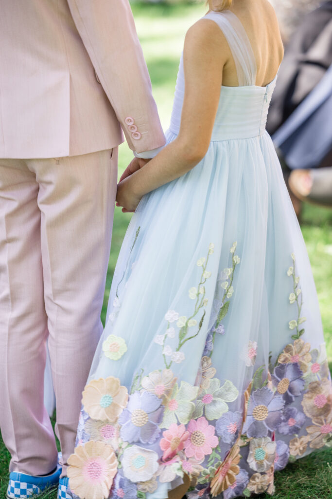 A close up detail of a flower girl's pale blue tulle gown embroidered with multicolored flowers in pinks, lavenders, and creams during a Napa Valley wedding at Beaulieu Gardens, photographed by Napa Valley wedding photographer Suzanne Karp