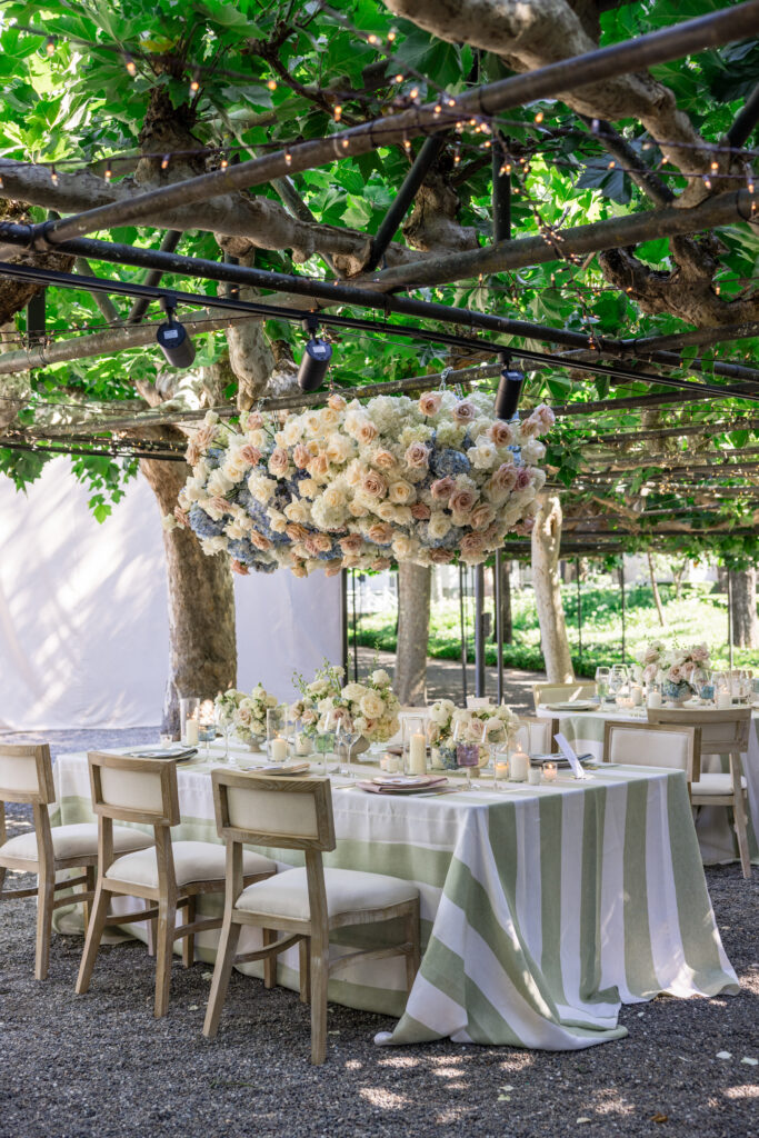 A lush hanging floral installation of cream garden roses, blush spray roses, and blue hydrangea suspended from the fig tree trellis above the reception dinner tables at Beaulieu Gardens in Rutherford, designed by Flowers by Edgar, photographed by Napa Valley wedding photographer Suzanne Karp
