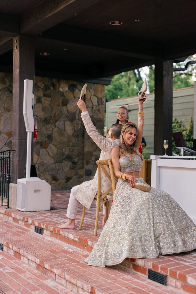 A bride raises a shoe triumphantly during the shoe game at her Sangeet celebration at Estate Yountville in Napa Valley, photographed by Suzanne Karp Photography