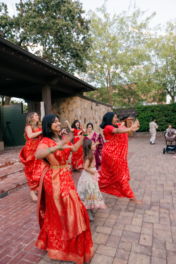 Bridesmaids in vibrant red banarasi sarees perform a choreographed dance on the brick courtyard during the Sangeet celebration at Estate Yountville in Napa Valley, photographed by Napa Valley wedding photographer Suzanne Karp