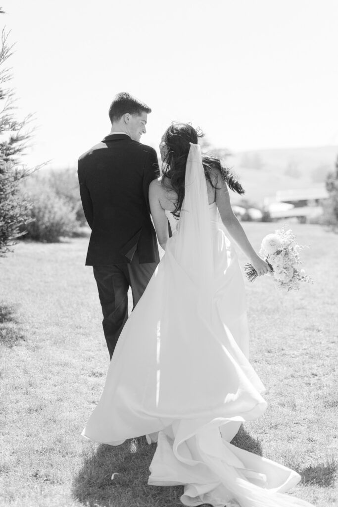 A black and white photograph of a bride and groom walking hand in hand across a sunlit lawn during their Northern California wedding portrait session, the bride's gown and veil flowing behind her, photographed by Napa Valley wedding photographer Suzanne Karp