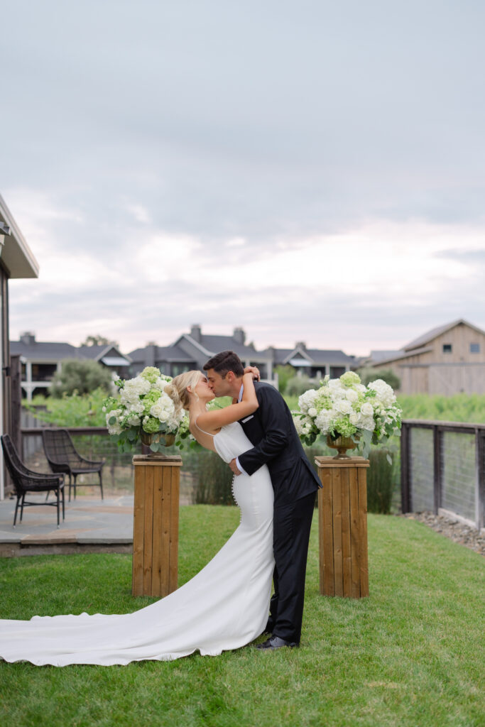 Groom dips his bride between the ceremony florals at dusk, her train sweeping the lawn at Four Seasons Napa Valley