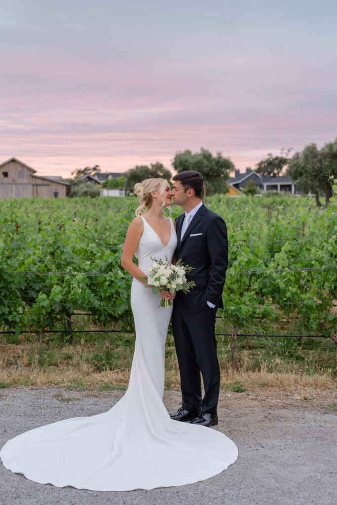 Newlyweds stand together in the vineyard under a pink sunset sky at Four Seasons Napa Valley in Calistoga
