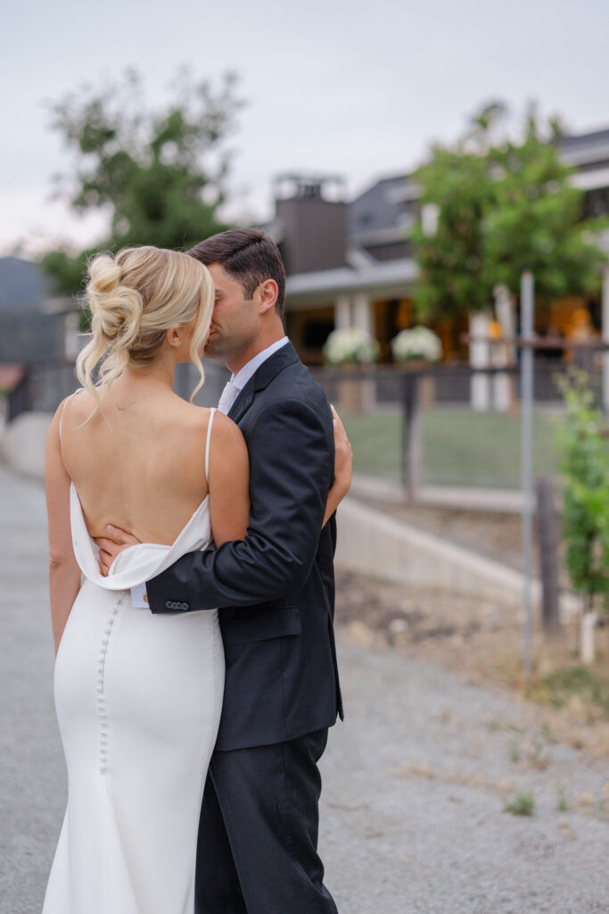 Groom kisses his bride's forehead, her cowl back gown catching the last light at Four Seasons Napa Valley