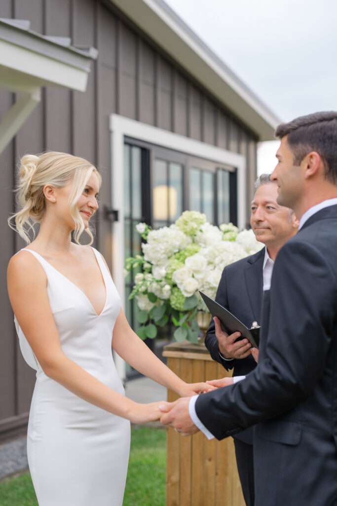 Couple holds hands as their officiant begins the ceremony at Four Seasons Napa Valley in Calistoga, framed by white hydrangea arrangements