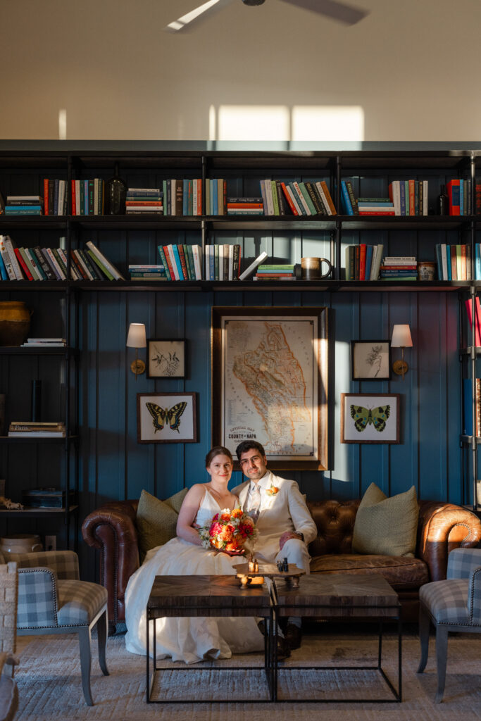 Newlyweds sit together in a navy library lounge with built-in bookshelves and warm lamplight during their Napa Valley elopement