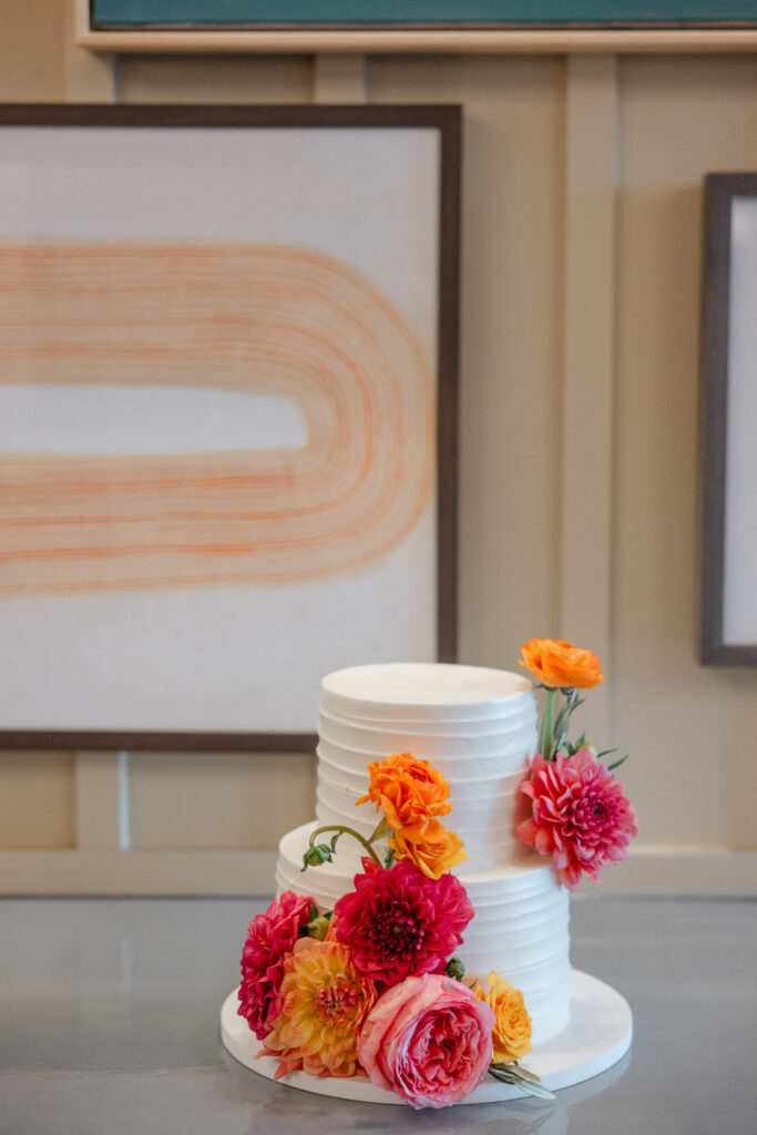 Two tier white wedding cake decorated with coral, orange and pink dahlias and garden roses