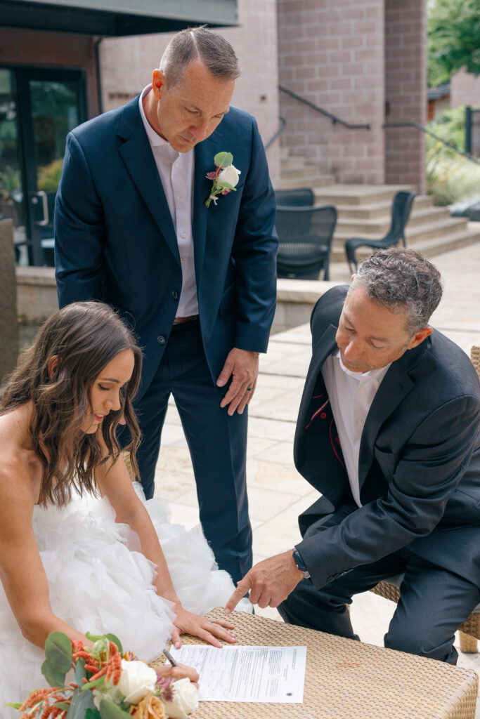 Bride signs her California marriage license on the patio at Bardessono while her husband and officiant Graham look on
